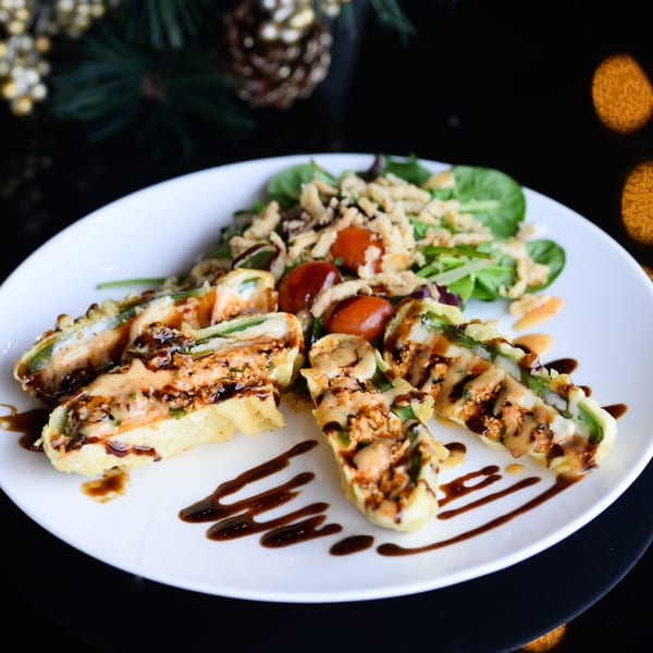Tempura-fried jalapeño poppers drizzled with sauce, served with a side salad on a white plate.