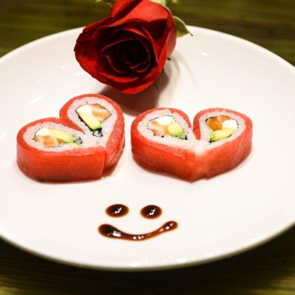 Heart-shaped sushi rolls with salmon and avocado, a red rose, and a soy sauce smiley face.