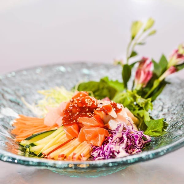 Colorful Asian salad with salmon, various vegetables, and a red sauce in a glass bowl.