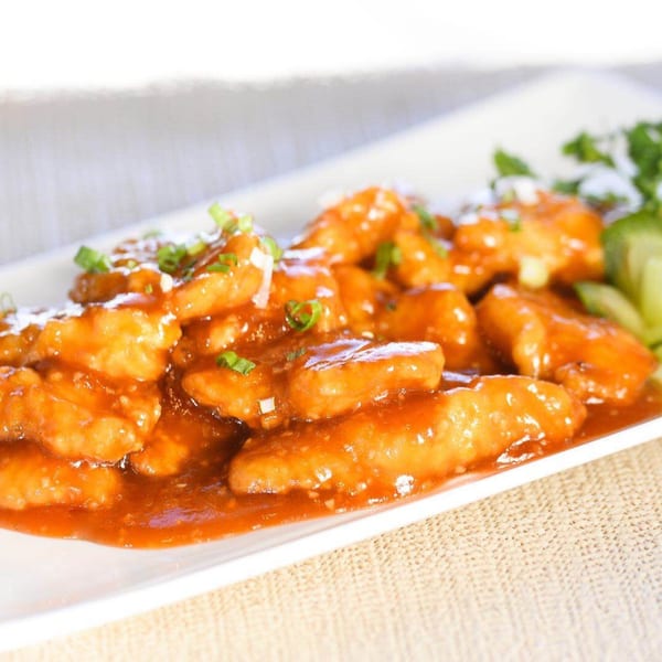 Sweet and sour chicken on a white rectangular plate, garnished with green onions and cilantro.