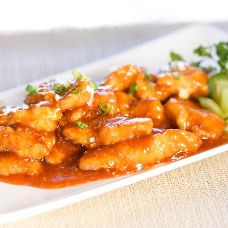 Sweet and sour chicken on a white rectangular plate, garnished with green onions and cilantro.