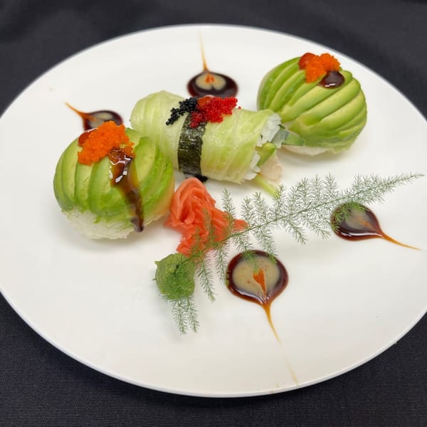 Three avocado-wrapped sushi rolls with roe, ginger, wasabi, and sauce on a white plate.