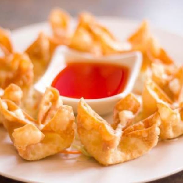 Crispy golden crab rangoon appetizers arranged around a small bowl of red dipping sauce.