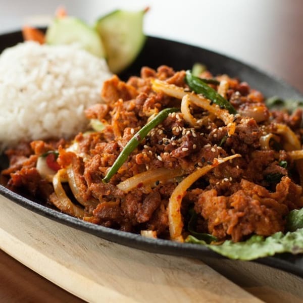 Spicy Korean BBQ pork with onions, green peppers, sesame seeds, and a side of white rice.