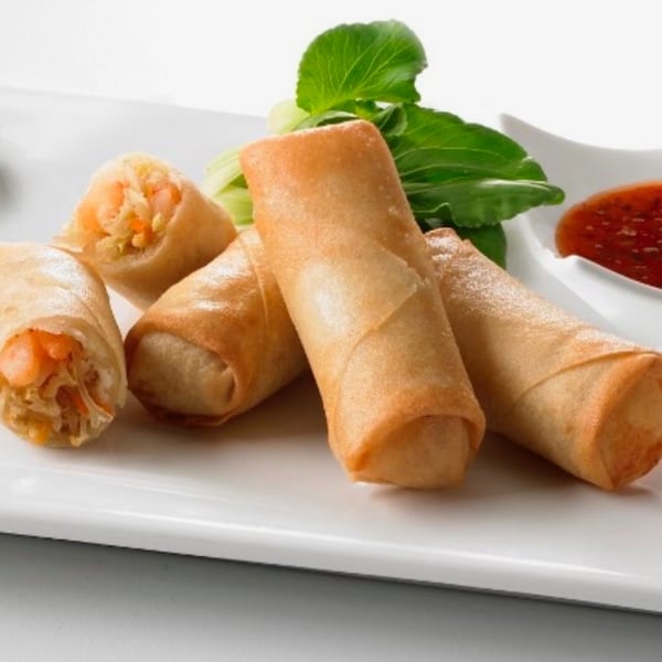Crispy golden spring rolls with a sweet chili dipping sauce and green garnish on a white plate.